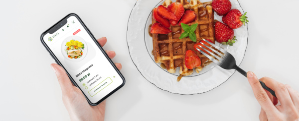 smartphone w dłoni z otwartym sklepem internetowym Konkret Dieta, obok talerz z gofrem i truskawkami