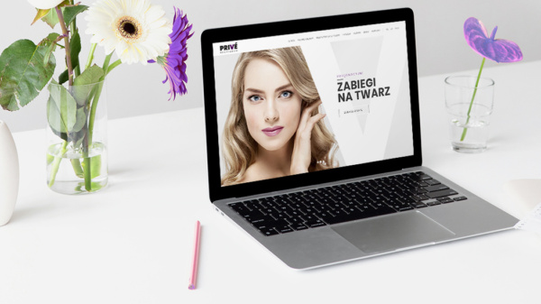 laptop z otwartą stroną internetową salonu kosmetycznego, w tle kwiaty w wazonach