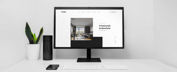 monitor z otwartą stroną internetową dewelopera Yakan Trade na biurku, obok kwiat