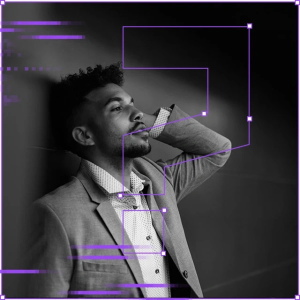 Zamyślony mężczyzna w garniturze, o ciemnej karnacji i kręconych włosach, opiera się o ścianę z ręką za głową. Nałożone fioletowe geometryczne efekty cyfrowe.