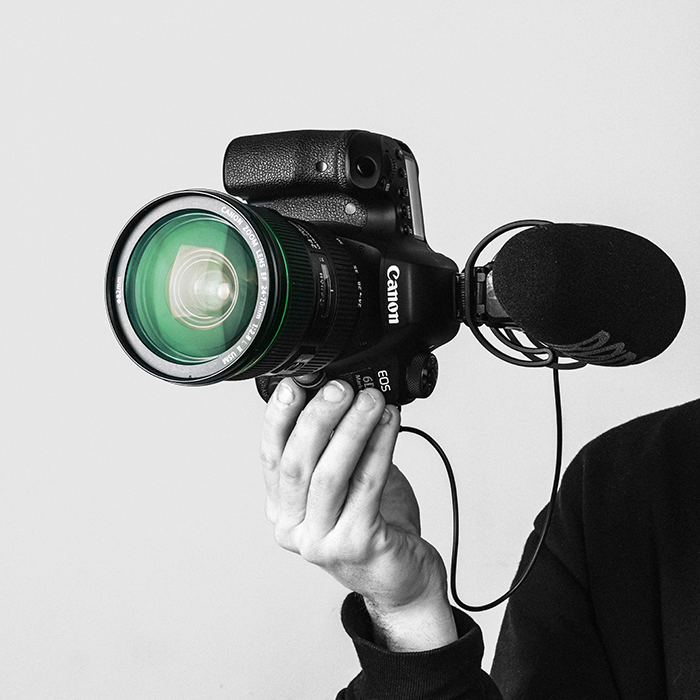 Ręka trzyma profesjonalny aparat Canon EOS z obiektywem i mikrofonem zewnętrznym