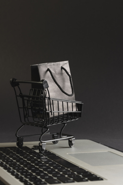Czarny koszyk zakupowy z torebką na klawiaturze laptopa, symbolizujący zakupy online i zmiany w e-commerce