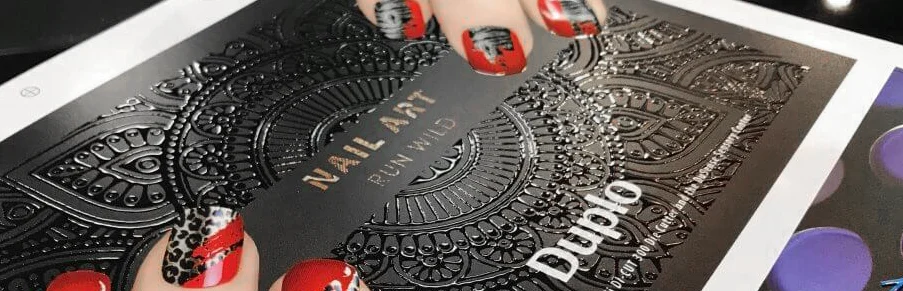 Dłonie trzymające czarną okładkę katalogu Nail Art z wypukłym lakierem sensorycznym 3D o wzorze mandali, wykonanym na maszynie Duplo DuSense