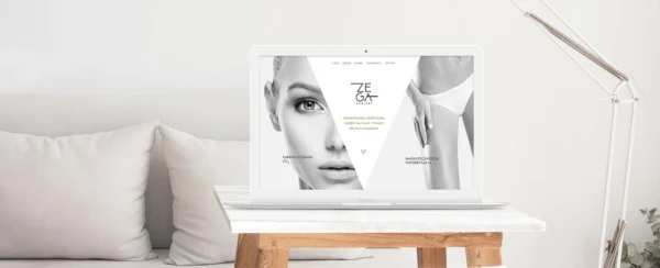 laptop z otwartą stroną internetową gabinetu kosmetologii estetycznej Zega na stoliku, w tle sofa