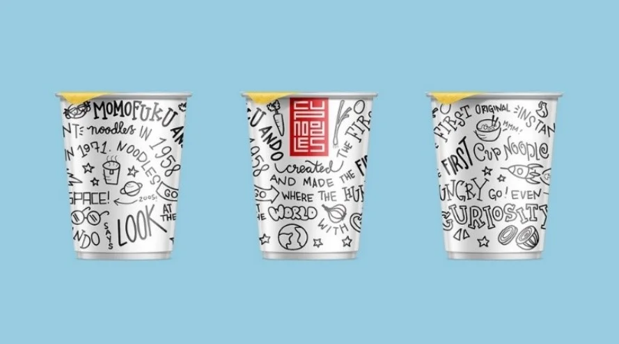 Trzy papierowe kubki na makaron Cup Noodles pokryte czarno-białymi rysunkami typu doodle