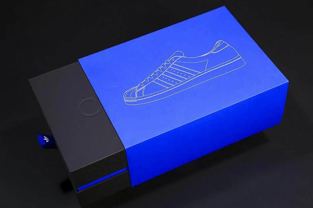 Niebiesko-czarne pudełko na buty Adidas z minimalną grafiką przedstawiającą szkic obuwia