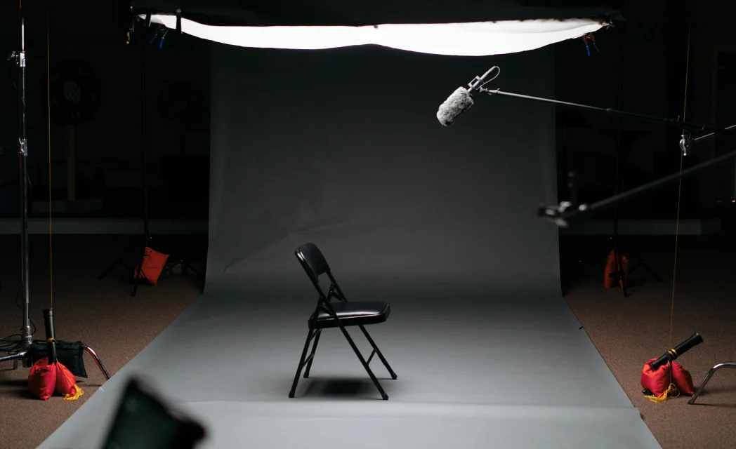 Profesjonalne studio nagrań wideo i podcastów z czarnym krzesłem na tle szarego cykloramy, profesjonalnym oświetleniem i mikrofonem kierunkowym na wysięgniku