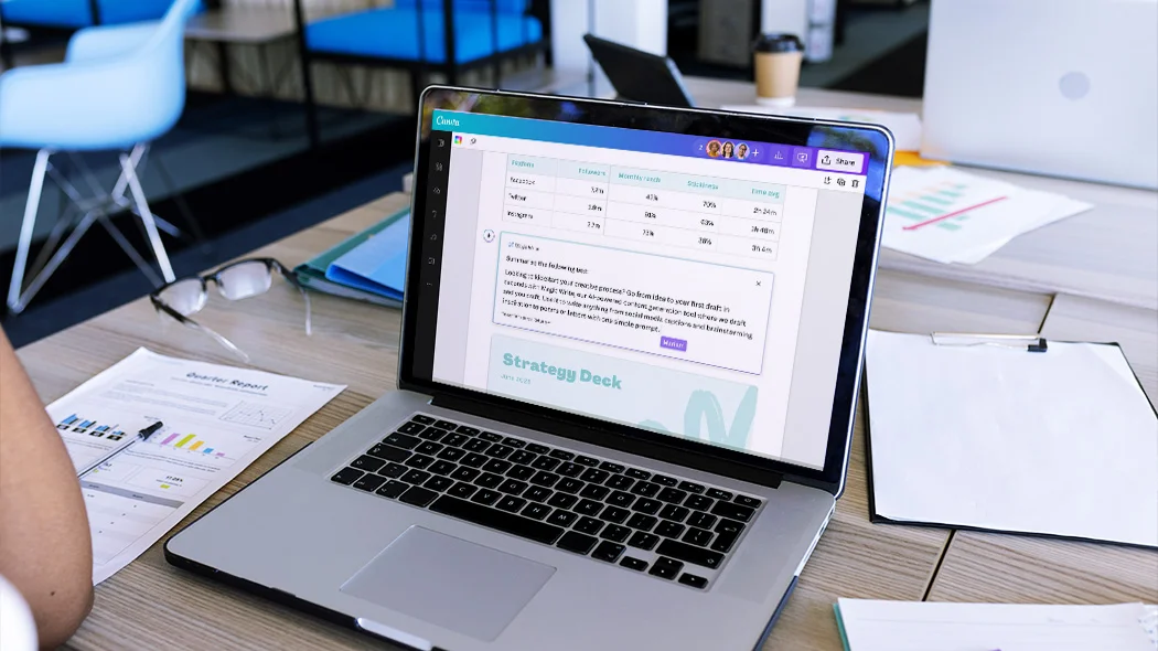 Otwarty laptop stojący na drewnianym biurku z uruchomioną aplikacją Canva, w której widoczna jest tabela z danymi social media oraz projekt prezentacji „Strategy Deck”.