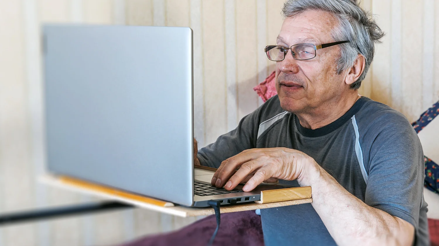 starszy mężczyzna z widoczną chorobą jednego oka korzysta samodzielnie z laptopa