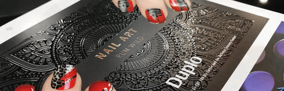 Dłonie trzymające czarną okładkę katalogu Nail Art z wypukłym lakierem sensorycznym 3D o wzorze mandali, wykonanym na maszynie Duplo DuSense