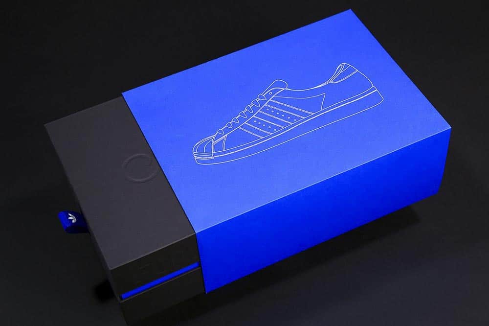 Niebiesko-czarne pudełko na buty Adidas z minimalną grafiką przedstawiającą szkic obuwia
