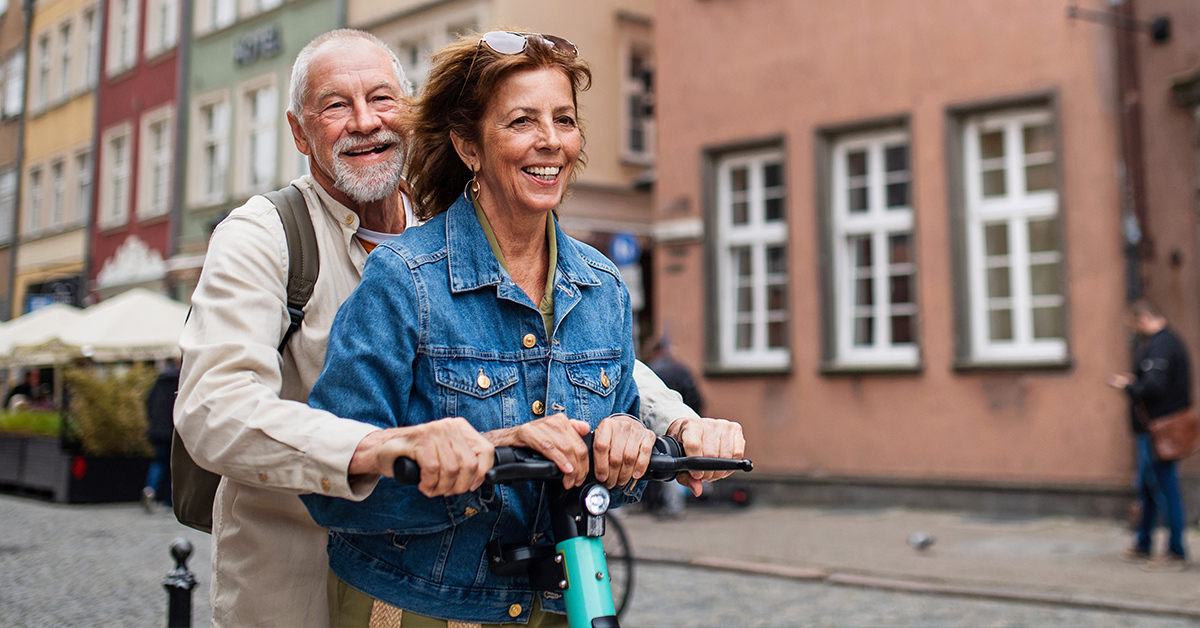Dwójka seniorów, mężczyzna i kobieta, podróżuje na hulajnodze elektrycznej