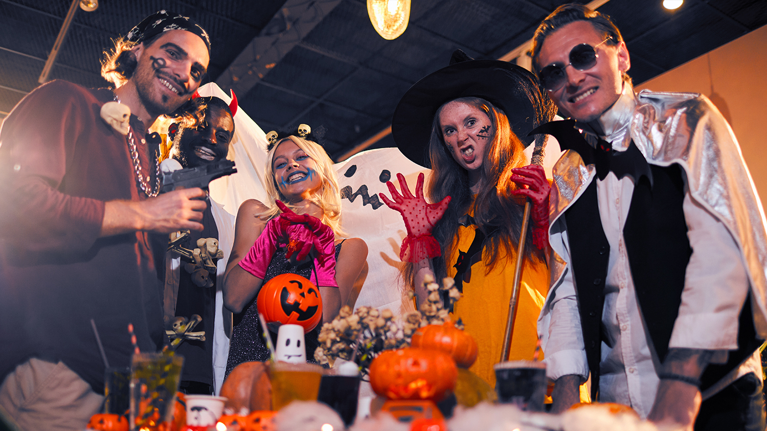 Impreza halloweenowa Grupa młodych ludzi przebrana w kostiumy halloweenowe stoi przy imprezowym stole