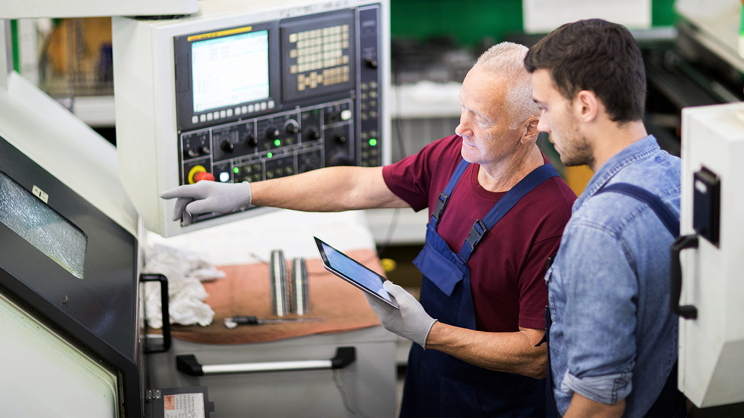 Starszy pracownik szkoli młodego adepta zawodu technicznego podczas wspólnej pracy przy maszynie
