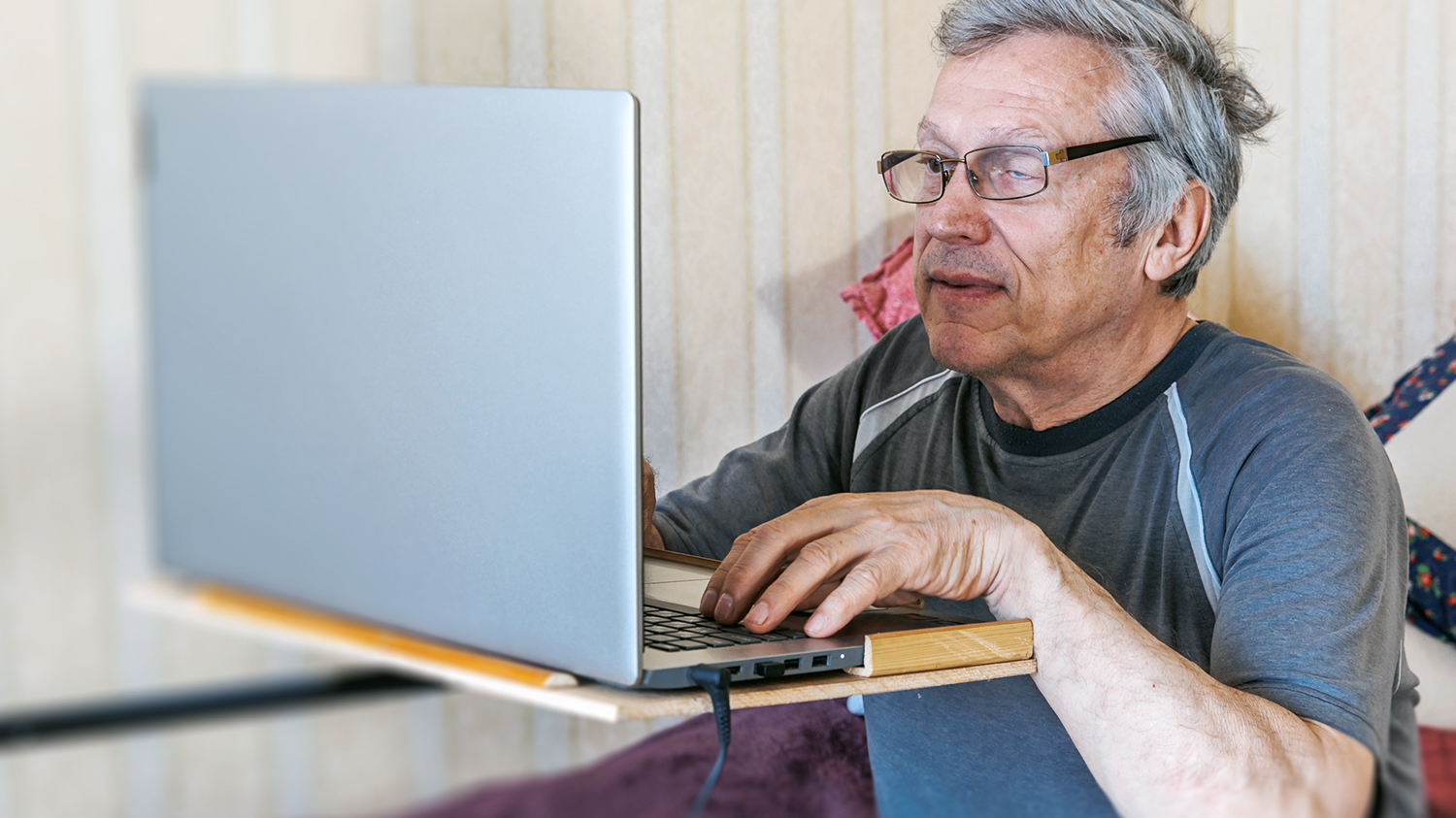 starszy mężczyzna z widoczną chorobą jednego oka korzysta samodzielnie z laptopa