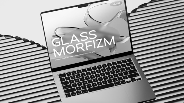 Laptop z otwartym ekranem pokazującym stronę internetową z napisem "GLASSMORFIZM" na tle abstrakcyjnych, szklanych kształtów. Laptop leży na powierzchni z czarno-białymi, poziomymi prążkami.
